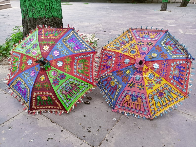 May include: Two colourful umbrellas with embroidered elephant designs and mirror accents. The umbrellas are made of fabric and have a fringe trim.