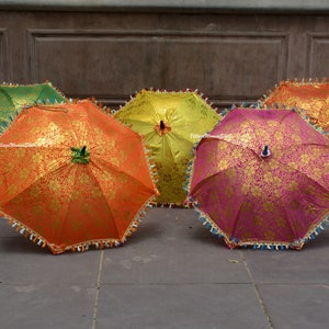 K&ouml;nnte beinhalten: F&uuml;nf dekorative, offene Regenschirme. Sie zeigen ein goldenes Blumenmuster auf orangefarbenem, gr&uuml;nem, gelbem und pinkfarbenem Hintergrund. Die R&auml;nder sind mit dekorativen Fransen versehen, was sie besonders macht.