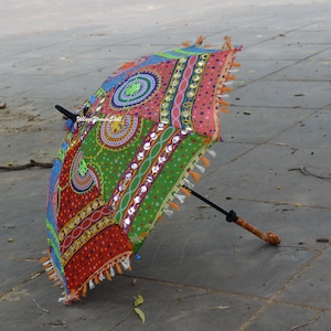 May include: A colorful, open umbrella with a patterned design. The umbrella features a mix of red, green, blue, and orange hues, with decorative tassels along the edges. The handle is brown and the frame is black.