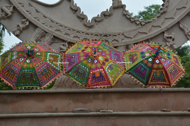 May include: Three colourful umbrellas with intricate embroidery and mirror embellishments. The umbrellas are decorated with floral patterns and elephant motifs.