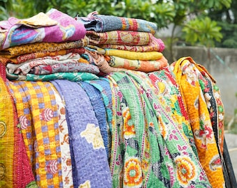 May include: A stack of colorful kantha quilts with various floral and geometric patterns. The quilts are made of recycled saris and are hand-stitched.