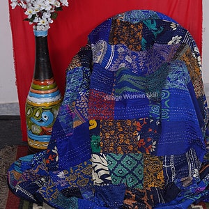 May include: A blue kantha quilt with a patchwork design featuring various floral and geometric patterns. The quilt is made of recycled saris and is hand-stitched. "Village Women Skill" is written on the quilt.