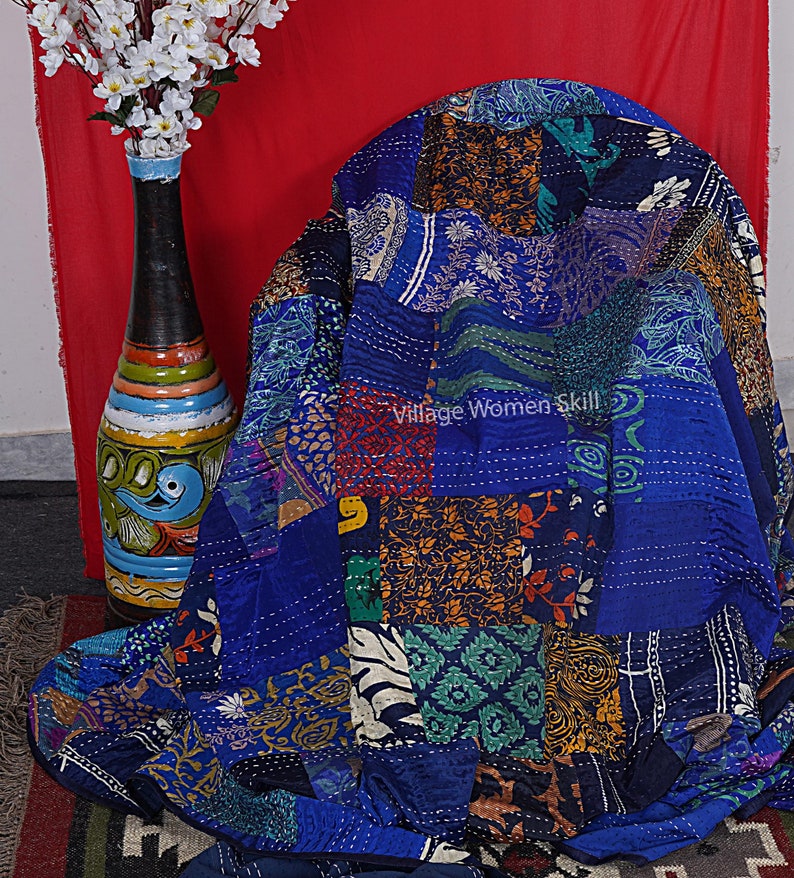 May include: A blue kantha quilt with a patchwork design featuring various floral and geometric patterns. The quilt is made of recycled saris and is hand-stitched. "Village Women Skill" is written on the quilt.