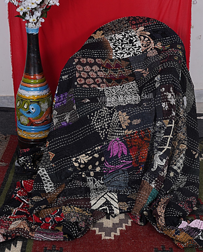 May include: Black kantha quilt with a patchwork design featuring various floral and geometric patterns. The quilt is hand-stitched with intricate details and has a vintage aesthetic.