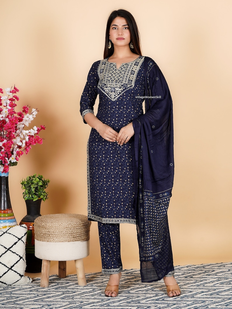May include: A navy blue salwar kameez with gold embroidery. The outfit includes a long-sleeved top, trousers, and a matching dupatta. The top features a V-neckline and intricate embroidery around the neckline and sleeves. The trousers are straight-leg and the dupatta is a sheer fabric with a gold border.