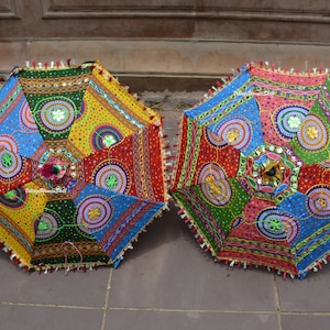 May include: Two colorful, open parasols with intricate patterns. The parasols feature a patchwork design with red, yellow, blue, and green panels, embellished with mirrors and tassels. The decorative umbrellas are likely for outdoor use.