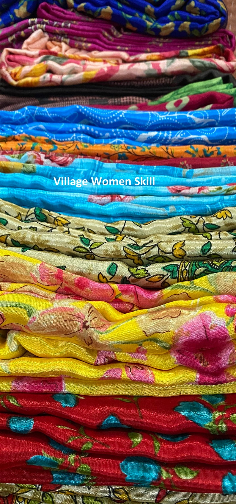 May include: A stack of colorful fabric with floral patterns. The fabric is folded and arranged in a rainbow pattern. The text "Village Women Skill!" is visible in the center of the image.