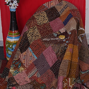 May include: A patchwork quilt made from various fabrics in shades of brown, pink, and blue. The quilt is folded and draped over a chair. The text "Village Women Skill" is visible on the quilt.