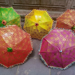 K&ouml;nnte beinhalten: Eine Auswahl an dekorativen Regenschirmen in verschiedenen Farben. Jeder Regenschirm hat ein goldenes Blumenmuster auf einem gr&uuml;nen, gelben, roten und rosa Hintergrund. Die R&auml;nder sind mit Quasten verziert.