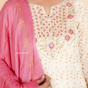 May include: White cotton kurta with a pink dupatta. The kurta has a gold and white floral print and a neckline with pink and gold embroidery. The dupatta has a gold and pink floral print.