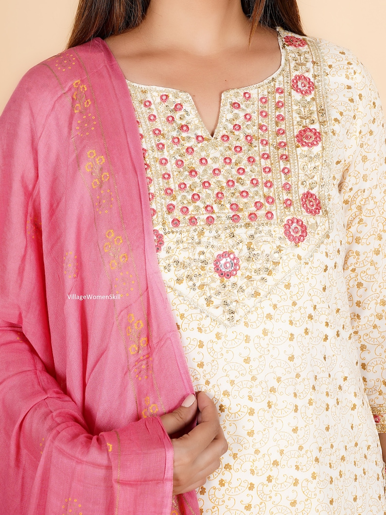May include: White cotton kurta with a pink dupatta. The kurta has a gold and white floral print and a neckline with pink and gold embroidery. The dupatta has a gold and pink floral print.