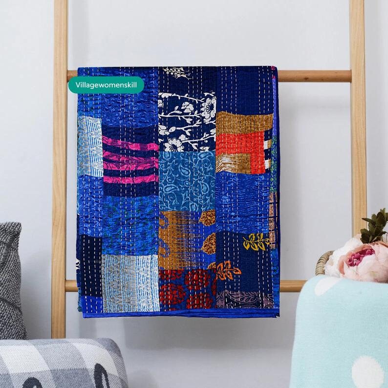 May include: A blue kantha quilt with a patchwork design featuring various colors and patterns, including floral, paisley, and geometric motifs. The quilt is hanging on a wooden ladder.