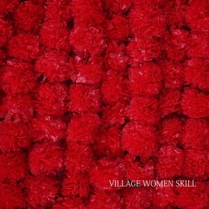 May include: A close-up image of a large quantity of red paper flowers. The flowers are arranged in a dense cluster, creating a vibrant and textured background. The text "VILLAGE WOMEN SKILL" is visible at the bottom of the image.