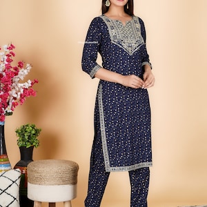 May include: A navy blue kurta and palazzo set with gold embroidery and a small white floral print. The set features a V-neckline and three-quarter sleeves.