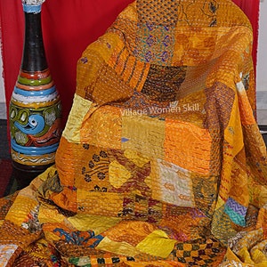 May include: A patchwork quilt made from a variety of yellow and gold fabrics. The quilt is hand-stitched and has a unique, rustic look. The quilt is draped over a chair and a vase of white flowers is in the background.