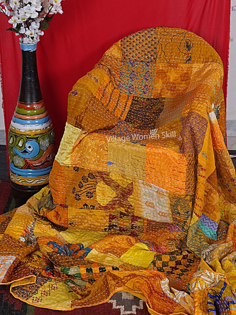 May include: A patchwork quilt made from a variety of yellow and gold fabrics. The quilt is hand-stitched and has a unique, rustic look. The quilt is draped over a chair and a vase of white flowers is in the background.
