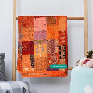Pu&ograve; includere: Un quilt patchwork con una variet&agrave; di tessuti arancioni, rosa e viola. Il quilt &egrave; composto da molti pezzi di tessuto diversi cuciti insieme in un motivo casuale. Il quilt &egrave; appeso a una scala di legno.