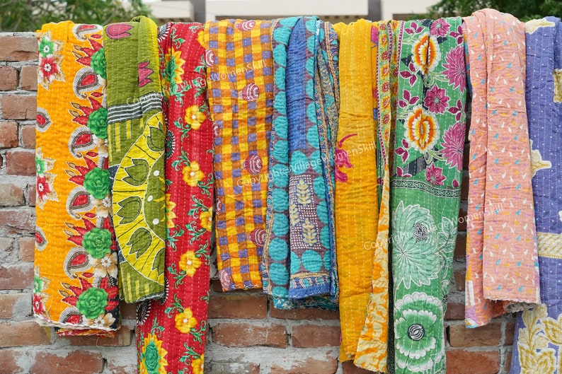 Puede incluir: Una colecci&oacute;n de colchas kantha coloridas colgadas en una pared de ladrillo. Las colchas est&aacute;n hechas de saris reciclados y presentan una variedad de patrones florales y geom&eacute;tricos.