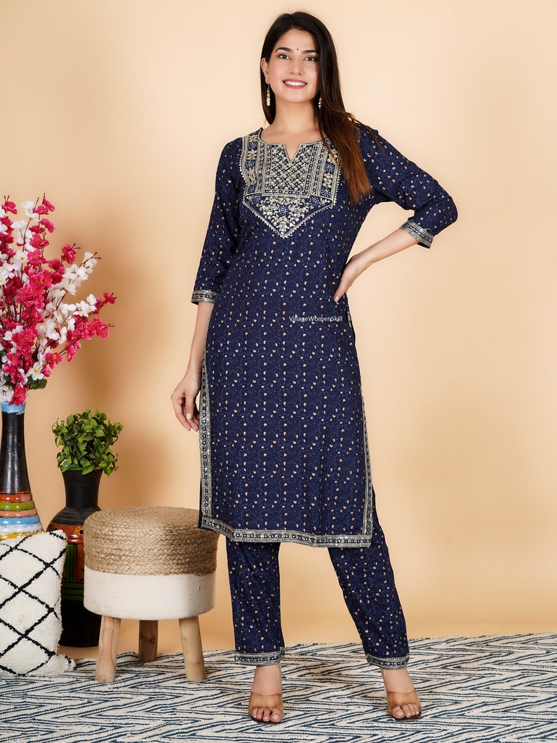 May include: A navy blue and gold patterned kurta and palazzo set. The kurta has a V-neckline and gold embroidery around the neckline. The palazzo pants have a wide leg and a gold trim around the bottom.