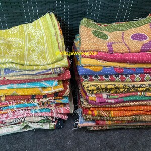 May include: A stack of colorful kantha quilts, made from recycled saris, with intricate patterns and stitching. The quilts are folded and stacked on a dark surface. @VillageWomenSkill