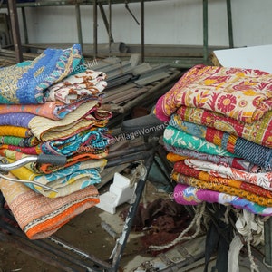 Puede incluir: Una pila de colchas kantha coloridas se apilan en una bicicleta, listas para la venta. Las colchas est&aacute;n hechas de saris reciclados y presentan intrincados patrones y dise&ntilde;os.