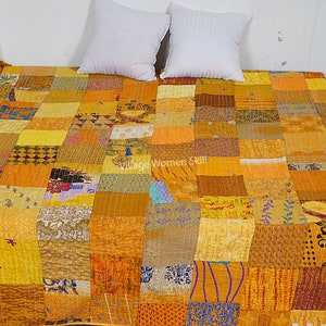 May include: A yellow and brown patchwork quilt with a variety of patterns. The quilt is made of many different fabrics and is hand-stitched. The quilt is laid out on a bed with two white pillows.
