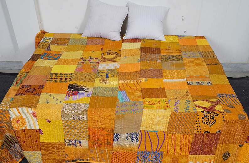 May include: A yellow and brown patchwork quilt with a variety of patterns. The quilt is made of many different fabrics and is hand-stitched. The quilt is laid out on a bed with two white pillows.