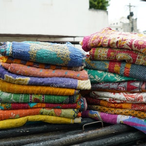Peut inclure: Une pile de courtepointes kantha colorées, fabriquées à partir de saris recyclés, avec une variété de motifs floraux et géométriques. Copyright@Village Womenskill.