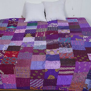 May include: Purple patchwork quilt with a variety of patterns and textures. The quilt is made of recycled saris and is hand-stitched.  "Vintage Women Skill" is printed on the quilt.