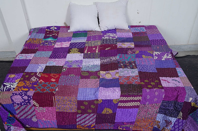 May include: Purple patchwork quilt with a variety of patterns and textures. The quilt is made of recycled saris and is hand-stitched.  "Vintage Women Skill" is printed on the quilt.