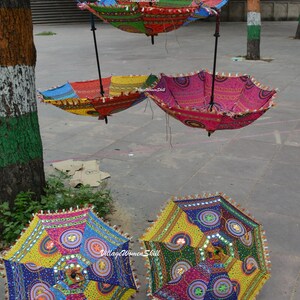 Puede incluir: Cuatro paraguas coloridos hechos a mano con adornos de espejo y flecos. Los paraguas est&aacute;n colgados de un soporte de metal negro. Los paraguas est&aacute;n hechos de tela y tienen una variedad de colores, incluyendo rojo, azul, verde, amarillo y rosa.