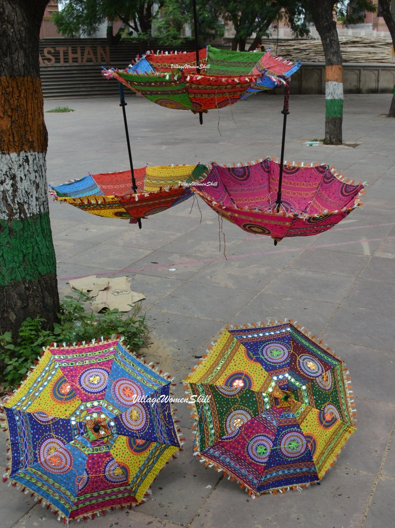 Puede incluir: Cuatro paraguas coloridos hechos a mano con adornos de espejo y flecos. Los paraguas est&aacute;n colgados de un soporte de metal negro. Los paraguas est&aacute;n hechos de tela y tienen una variedad de colores, incluyendo rojo, azul, verde, amarillo y rosa.