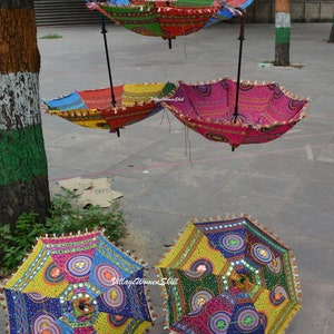 May include: A collection of colorful, decorative umbrellas with intricate patterns and mirror accents. The umbrellas are suspended in the air, showcasing a variety of vibrant colors including pink, blue, yellow, and green. Each umbrella has a diameter of approximately 30 inches.