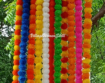 Könnte beinhalten: Ein Set aus zehn bunten Girlanden aus Stoffpompons. Die Girlanden sind in den Farben Blau, Orange, Gelb, Weiß, Grün und Pink gehalten. Die Girlanden hängen an einem Baumzweig.