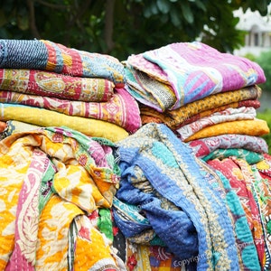 Puede incluir: Una pila de colchas kantha coloridas, hechas de saris reciclados, con una variedad de patrones florales y geom&eacute;tricos. Las colchas est&aacute;n dobladas y apiladas una encima de la otra, creando una exhibici&oacute;n vibrante y texturizada.