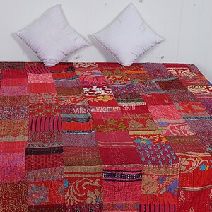 May include: Red and pink patchwork quilt with a variety of floral and geometric patterns. The quilt is made of recycled saris and is hand-stitched. "Village Women Skill" is printed on the quilt.