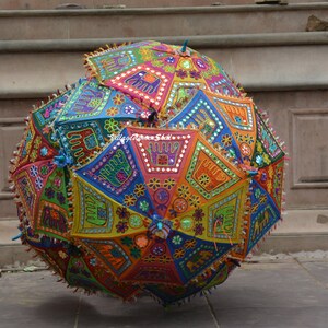 May include: A colourful, round, fabric umbrella with intricate embroidery and mirror work. The umbrella is decorated with geometric patterns, floral motifs, and small mirrors. The umbrella is a vibrant mix of red, orange, yellow, green, blue, and purple.