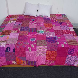 May include: A pink and purple patchwork quilt with a variety of patterns and textures. The quilt is made of recycled saris and is hand-stitched. The quilt is laid out on a bed with two white pillows.