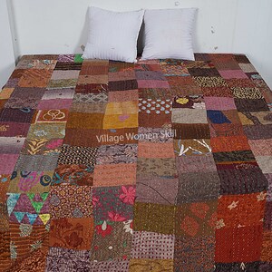 May include: A patchwork quilt made from a variety of fabrics in shades of brown, pink, and purple. The quilt is made up of squares of different sizes and patterns, and it has a rustic, handmade look. The quilt is laid out on a bed with two white pillows.