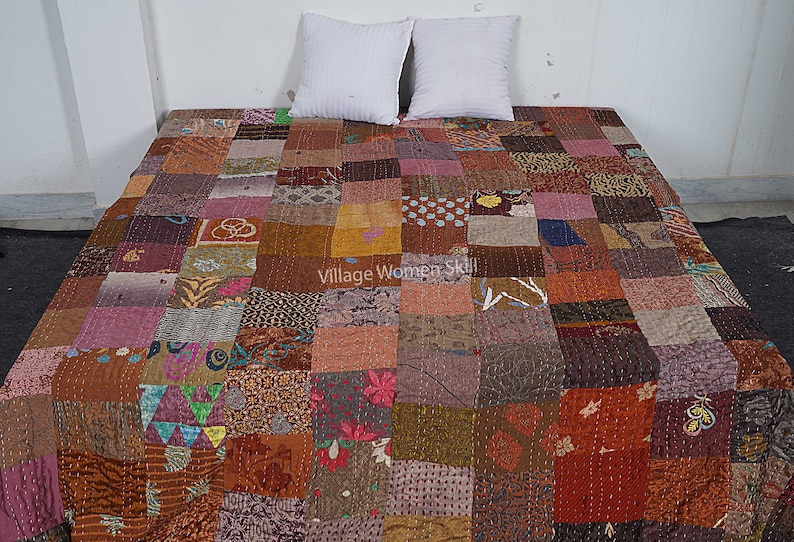 May include: A patchwork quilt made from a variety of fabrics in shades of brown, pink, and purple. The quilt is made up of squares of different sizes and patterns, and it has a rustic, handmade look. The quilt is laid out on a bed with two white pillows.