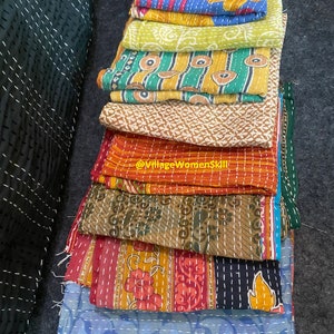 May include: A stack of colorful kantha quilts with intricate embroidery and patterns. The quilts are made of recycled saris and are a traditional Indian craft.
