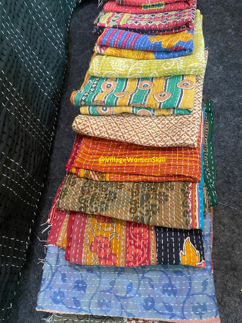 May include: A stack of colorful kantha quilts with intricate embroidery and patterns. The quilts are made of recycled saris and are a traditional Indian craft.