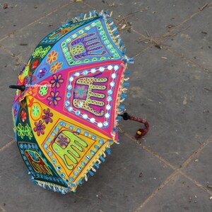 May include: A colourful umbrella with embroidered elephants and floral designs. The umbrella is made of fabric and has a wooden handle.