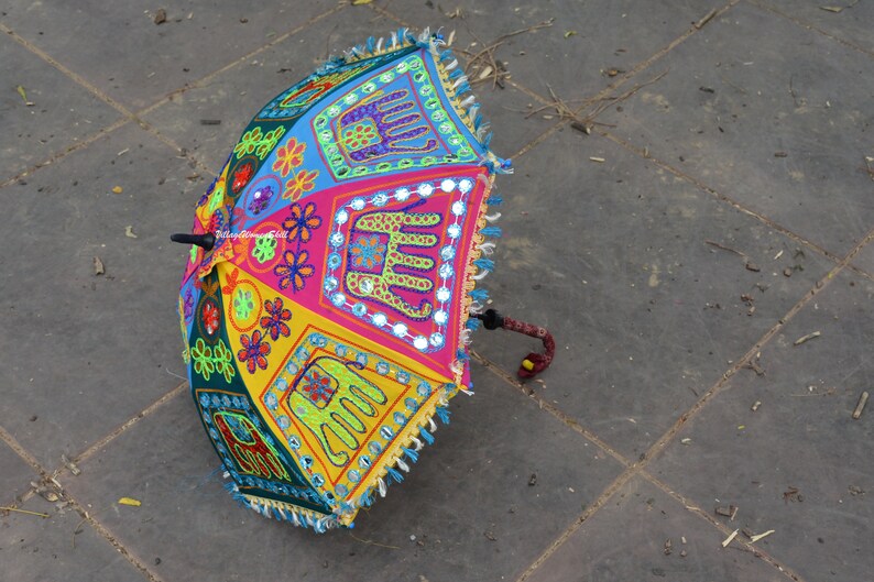 May include: A colourful umbrella with embroidered elephants and floral designs. The umbrella is made of fabric and has a wooden handle.