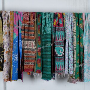 May include: A collection of colorful kantha quilts, also known as kantha stitch quilts, hanging on a white wall. The quilts are made of recycled saris and feature a variety of patterns and colors, including blue, green, pink, and yellow.  The quilts are all hand-stitched and have a unique, vintage look.