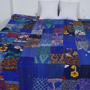 May include: A blue kantha quilt with a patchwork design made from various fabrics. The quilt is made up of squares of different colors and patterns, including floral, geometric, and paisley designs. The quilt is laid out on a bed with two white pillows.