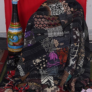 May include: Black kantha quilt with a patchwork design featuring various floral and geometric patterns. The quilt is hand-stitched with intricate details and has a vintage aesthetic.