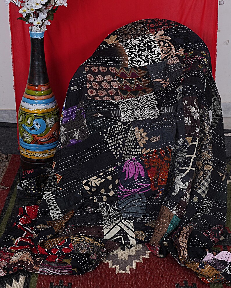 May include: Black kantha quilt with a patchwork design featuring various floral and geometric patterns. The quilt is hand-stitched with intricate details and has a vintage aesthetic.