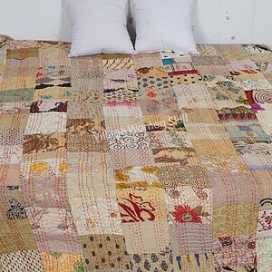 May include: A patchwork quilt made from a variety of fabrics in shades of beige, brown, and cream. The quilt is hand-stitched and has a unique, rustic look. "Village Women Skill" is printed on the quilt.