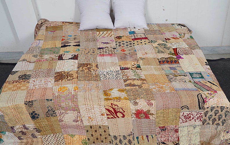May include: A patchwork quilt made from a variety of fabrics in shades of beige, brown, and cream. The quilt is hand-stitched and has a unique, rustic look. "Village Women Skill" is printed on the quilt.